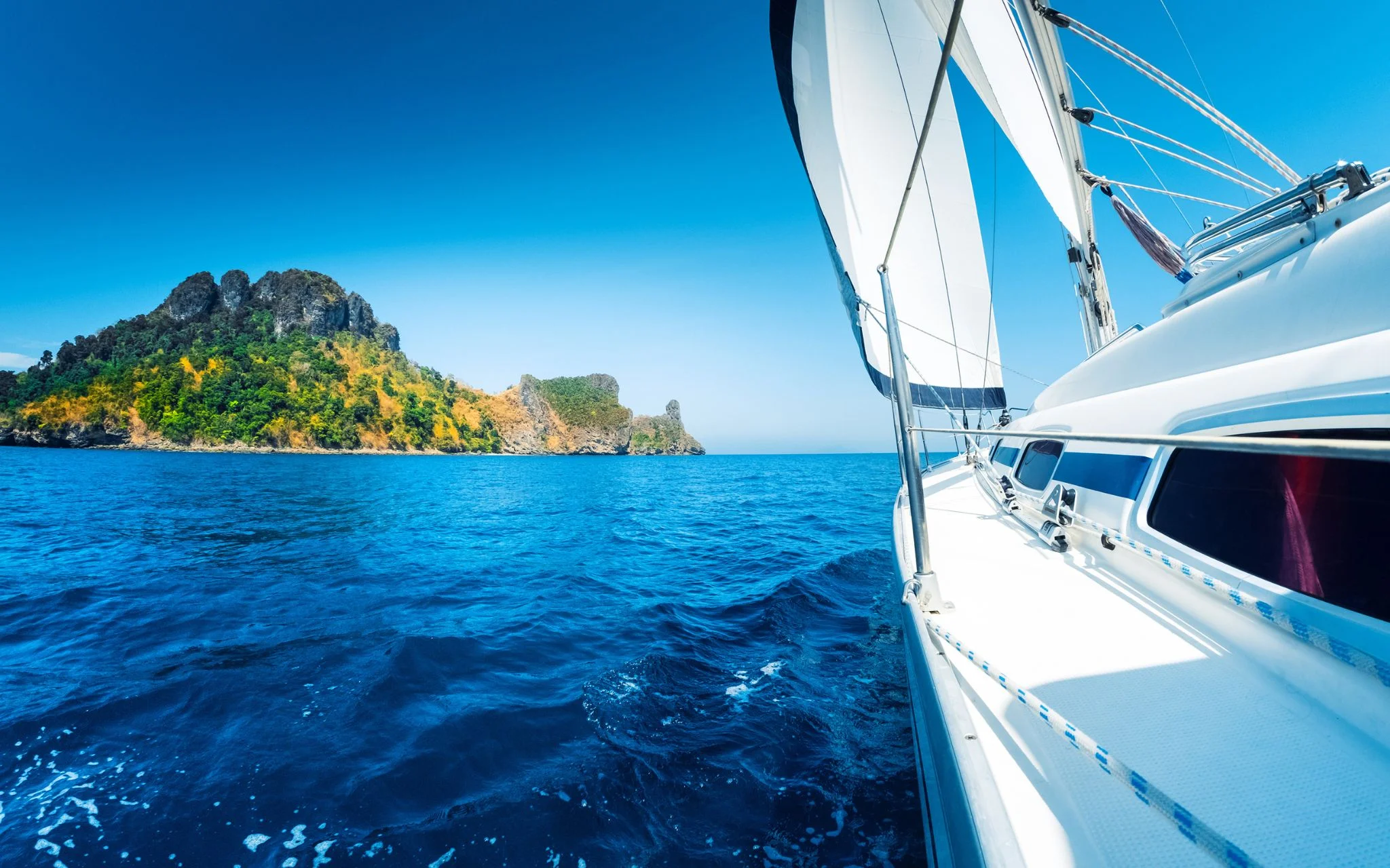 A stunning view of the crystal-clear turquoise waters of the Aegean Sea with rocky islands in the distance. A small boat is visible on the water, surrounded by the beautiful landscape of the Cyclades, Greece.